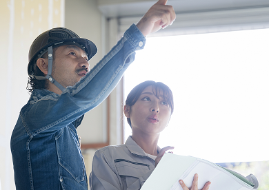 リフォーム現場で図面を手に天井の施工箇所を指差して打ち合わせをする建築スタッフ